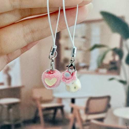 Hand holding flocked apple and apple core phone charms against cafe blur