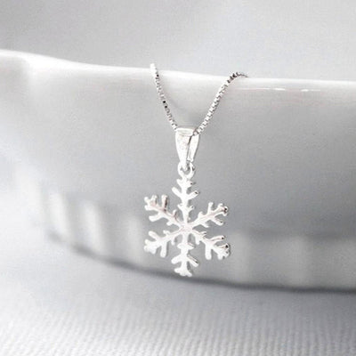 Silver snowflake pendant on fine box chain draped over white ceramic bowl