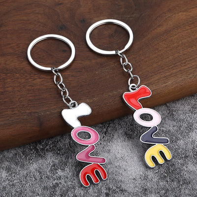 Two vertical LOVE keychains with white and red top letters rest on a wood and gray fabric surface.