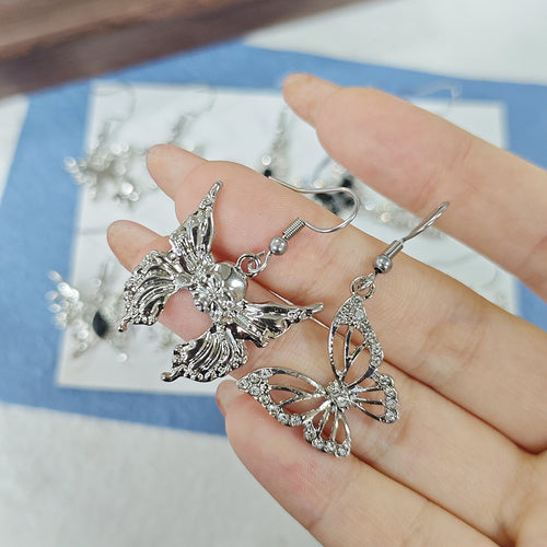 Two silver butterfly earrings held in hand showing sculpted and openwork styles