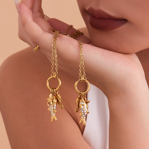 Model holding two gold fish ocean charm necklaces