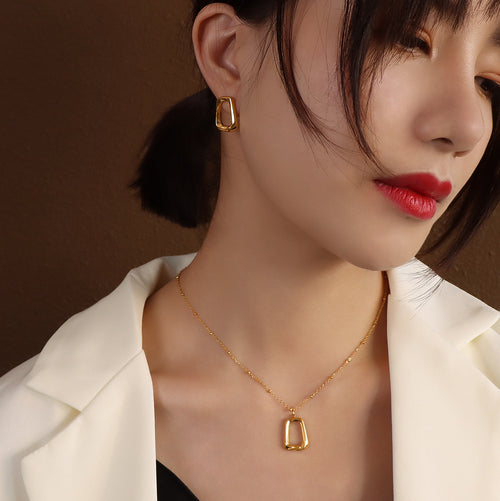 Model in white blazer wearing gold open square pendant and stud