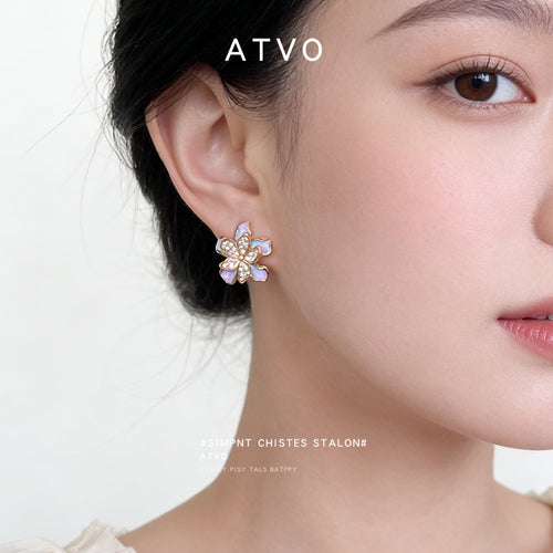 Gold-tone iridescent-lavender clear-stone flower studs shown worn on an ear.