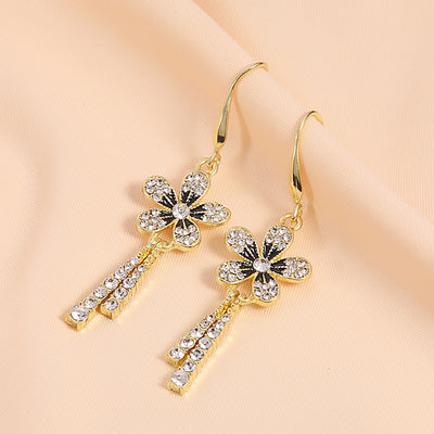 Gold rhinestone flower drop earrings angled on peach fabric