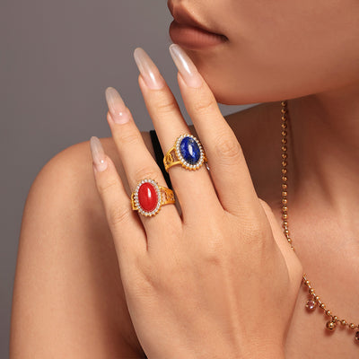 Hand wearing gold open rings with red and deep blue oval stones in zircon halos