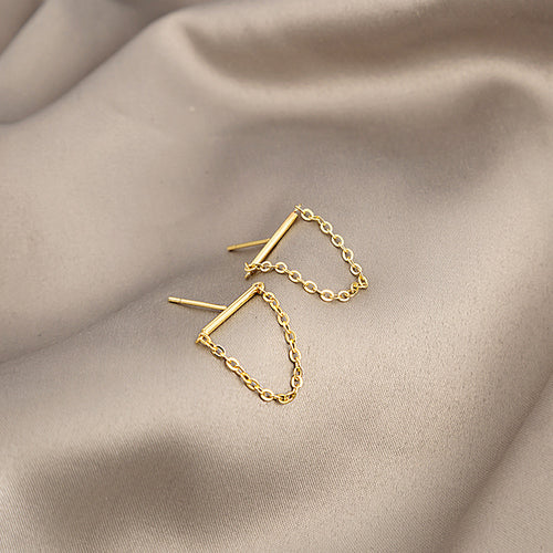Gold bar stud earrings with chain loops angled on beige fabric