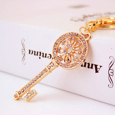 Close-up of a gold-tone key charm decorated with clear stones and floral openwork.
