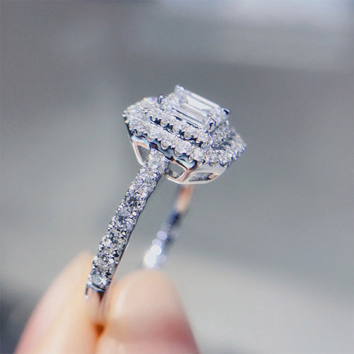 Styled view showing an emerald-cut center with a clear halo and slim stone-set band