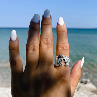 Silver wave cutout metal ring worn outdoors by blue sea background