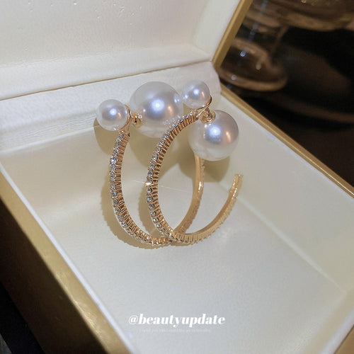 Styled close-up of gold tone pearl double hoop earrings