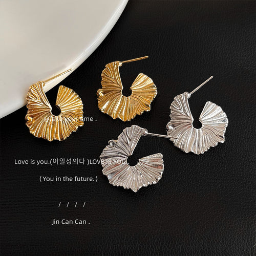 Four gold and silver fan leaf studs on black leather surface