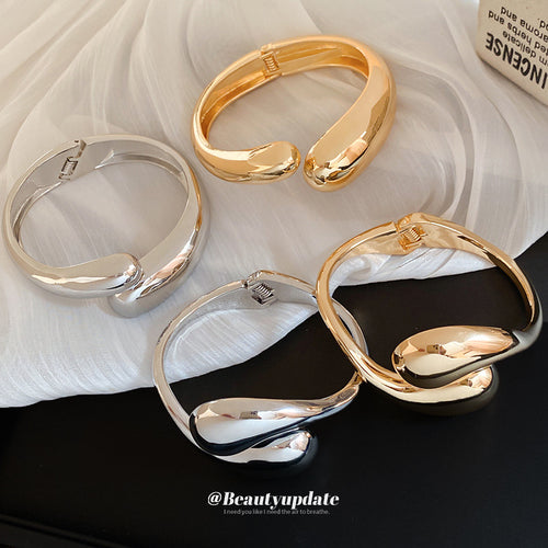 three gold-tone or silver-tone open hinged bracelets with smooth teardrop ends shown in the first close product view
