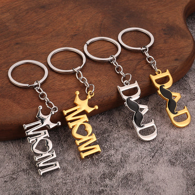 Four silver-tone and gold-tone MOM and DAD keychains displayed on a wooden surface.
