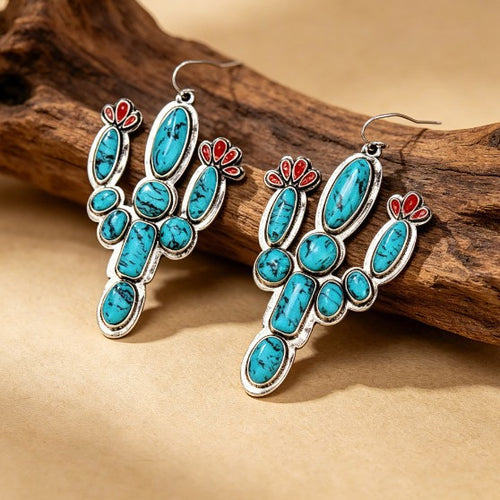 Pair of turquoise-color cactus and red flower earrings arranged on a warm neutral surface