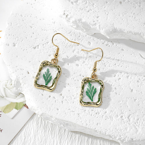 Green leaf dried resin gold ornate frame fishhook earrings pair on white stone