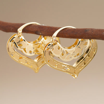 Gold hollow heart filigree hoop clip earrings hanging on brown twig