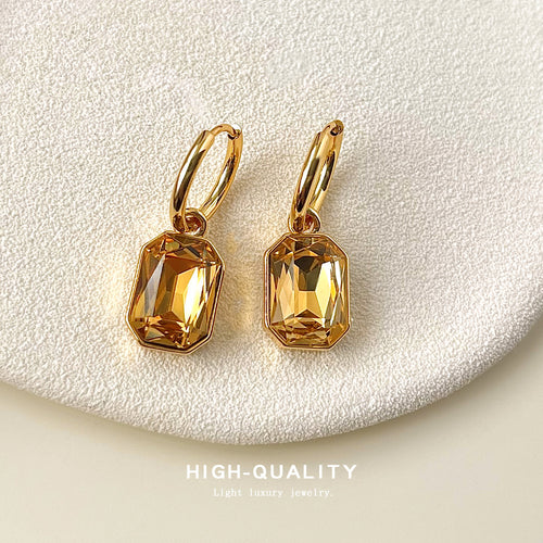 Gold-tone amber-rectangle-stone huggie drops shown worn on an ear.