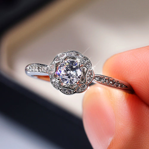 Silver flower halo CZ ring angled near dark jewelry box