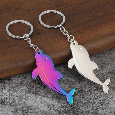 Two dolphin keychains in silver-tone and iridescent finishes rest on wood and gray fabric.