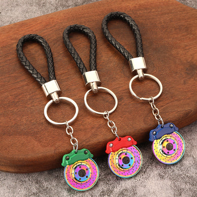 Three brake disc keychains with green, red, and blue calipers rest on a wooden board.