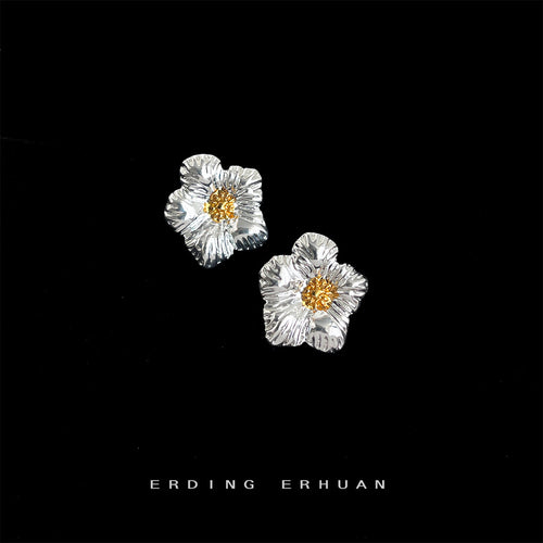 Silver textured flower studs with gold centers on black backdrop