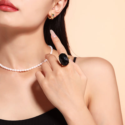Black large oval glass ring worn on finger with pearl necklace