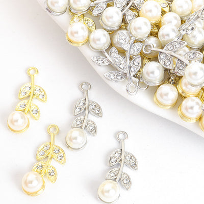 Assorted pearl and crystal leaf branch charms arranged beside a tray on white