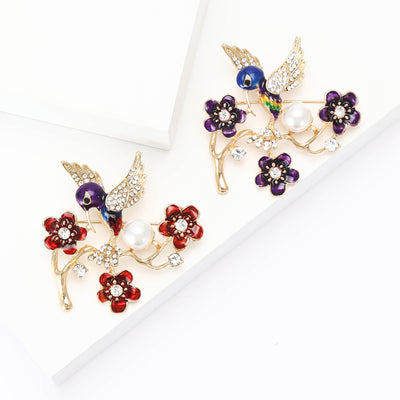 Front view of purple bird perched among enamel flowers and a white pearl-like bead