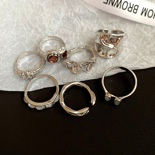 Seven mixed sculptural silver rings with stones on white paper surface