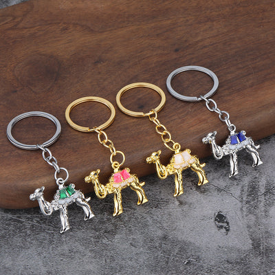 Four camel keychains display pink, white, blue, and green saddle details in gold-tone and silver-tone finishes.