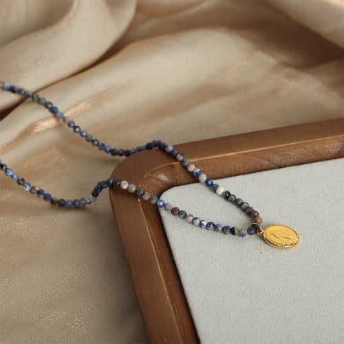 Bead necklace with gold oval medal on wood tray edge