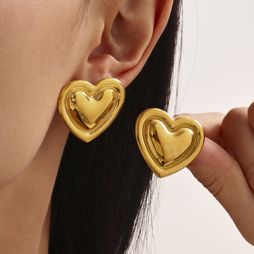 Model wearing large polished gold puffy heart stud earrings