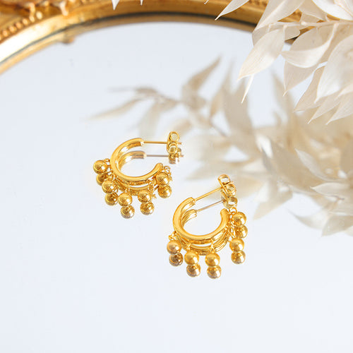 Pair of gold C hoop ball-bead earrings on mirrored surface with dried florals