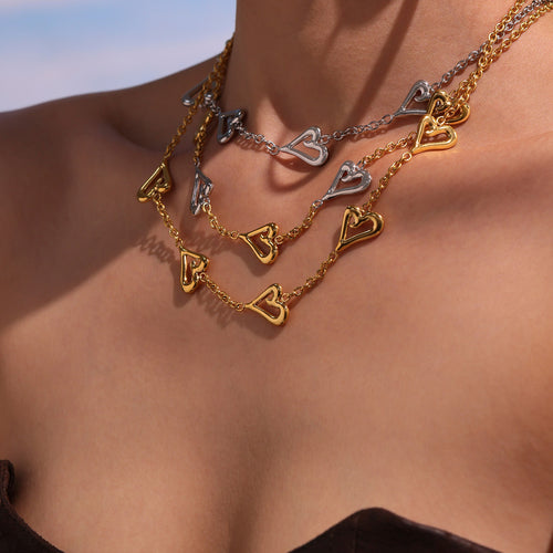 Close neck view of stacked gold and silver open-heart necklaces