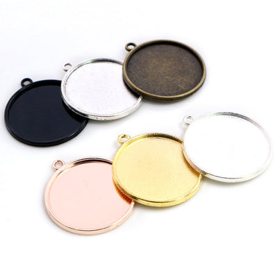 Overview of smooth round pendant trays with single top loops in black, gold, silver, rose and bronze tones arranged on a