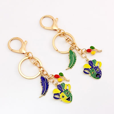 Two jester mask keychain colorways displayed together with green and blue feathers
