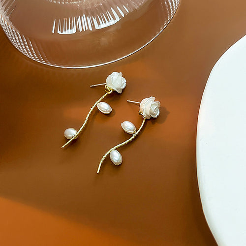 White rose post earrings with pearl branch drops on amber surface