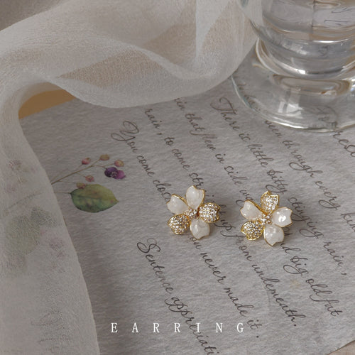 White and pave flower studs on script paper under gauze