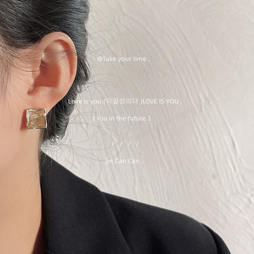 Gold-tone translucent coffee-brown square studs shown worn on an ear.