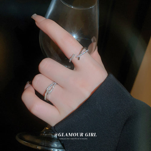 two silver-tone open rings with crossing clear crystal bands shown worn in a styled second view