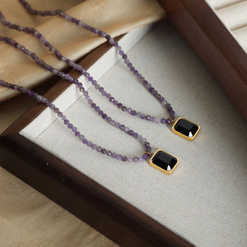 Two purple bead necklaces with black square pendants in jewelry tray