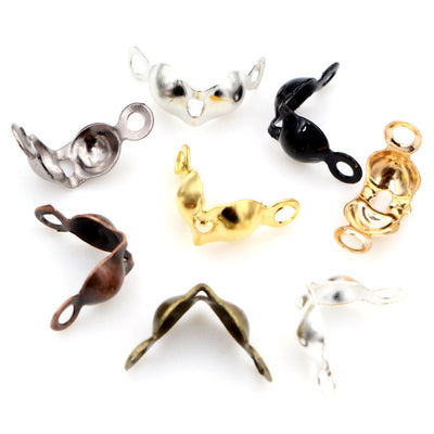 Overview of small paired-leaf fold-over bead tips with hanging eyes in silver, gold, black and bronze tones arranged on 