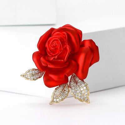 Front view of sculpted red rose brooch with three crystal-covered gold leaves against a white background.