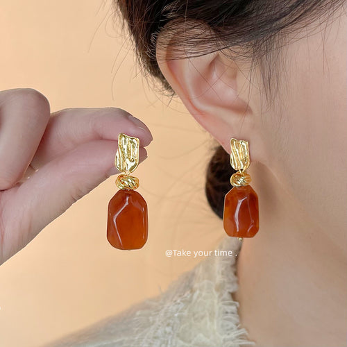 Gold amber stone drop earring worn on ear while matching piece held