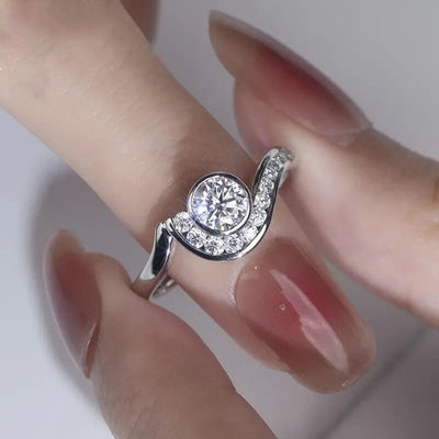 silver tone ring showing round clear center stone wrapped by a curved accent band