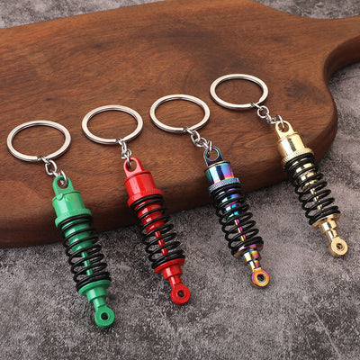 Four miniature shock absorber keychains in green, red, multicolor, and gold finishes.