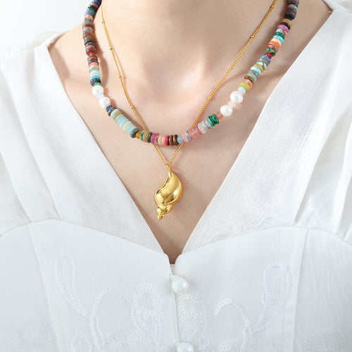 Model in white blouse wearing gold conch pendant layered with multicolor beads
