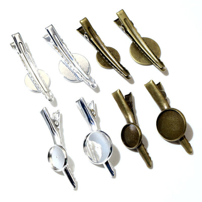 Front overview of metal alligator hair clip blanks with round bezel trays arranged on a light background