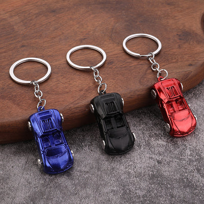Three car keychains in blue, black, and red on a wood and fabric surface.