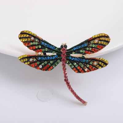 Front view of the multicolor dragonfly brooch showing a long-winged dragonfly outlined in dark crystals with multicolor 